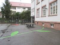Schulhof mit Bodenverzierungen, und einer Tischtennisplatte, rechts das Gebäude Neckarschule
