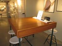 Ein hochgestellter Tisch mit einem braunen Holzaufsatz. Um den Tisch stehen mehrere höhere Hocker.