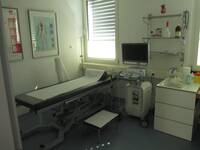 Eine Raum mit Liege und medizinischen Geräten, rechts am Bildrand steht ein Schreibtisch