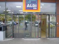 Glasfront mit automatischer Glasschiebetür und Windfang, darüber Aldi-Logoren des Ein- und Ausgangs befinden, über den Türen ist das ALDISchild angebracht