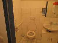 Ein weiße Behindertentoilette mit einem weißen Waschbecken in einem weiß gefliesten Raum