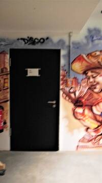 Dunkle Tür in grauer Wand, rechts buntes Graffiti