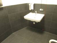 Ein weißes Waschbecken an einer schwarz gekachelten Wand. Über dem Waschbecken sind zwei Seifenspender