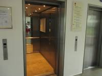 offenstehender Aufzug, Kabine mit Handlauf rechts und Spiegel an der Rückwand. Rechts und links an der weißen Wand sind Tasten.