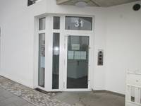 Hausecke mit Glastür in einer weißen Wand, rechts neben der Tür Metallplatte mit Bedienelementen