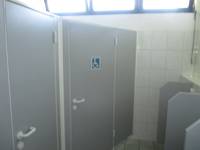 breite Kabinentür mit einem blauen Rollstuhlsymbol, links weitere Toilettentür, rechts Pissoirs