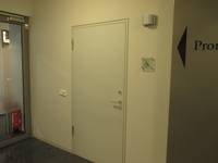  weiße Tür in einer weißen Wand. Rechts davon ein Schild mit Rollstuhlsymbol