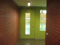Tür mit schmaler Glasscheibe, rechts davon Einblick in die Halle