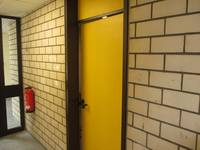 gelbe Tür in einer gemauerten Wand, links Feuerlöscher