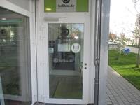 Glastür in weißem Metallrahmen, über der Tür ist das Logo von brillen.de in einer hellgrünen Glasfläche.