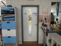 helle einflügelige Tür mit einem dunklen Rahmen, links und rechts Regale mit verschiedenen Sportutensilien