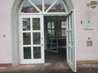 Zweiflügelige gläserne Eingangstür mit Bogen, Holzrahmen und Streben in, der rechte Flügel steht offen, dahinter Windfang