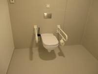 Weiße Toilette mit Haltegriffen auf beiden Seiten in einem deckenhoch gefliesten Raum