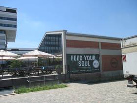 Eckgebäude mit Giebeldach, an der Giebelseite eine Glasfront, daran anschließend Terasse, an der Backsteinwand ein großes Plakat mit dem Spruch "Feed your Soul"