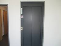 dunkelgraue Aufzugstür in weißer Wand, links daneben Flur EG zu Behindertentoiletten