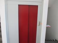 geschlossene  rote Aufzugtür in einer weißen Wand, rechts an der Wand Taster