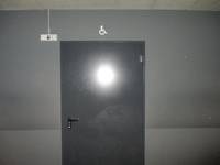dunkle Tür, darüber ein Rollstuhlsymbol, Wand darum herum ist grau
