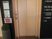 Geschlosener Aufzug mit gutem Kontrast zur umgebenden Wand. Rechts vom Aufzug Hinweise mit richtungsweisenden Pfeilen z.B. zu Toiletten