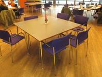 eine Tischgruppe bestehend aus zwei Tischen mit sechs blauen Stühlen ohne Armlehne, im Hintergrund weitere Tischgruppen