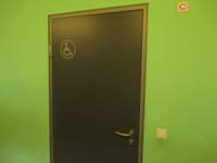 dunkle Tür in einer grünen Wand, auf der Tür Rollstuhlsymbol