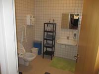 Toilette, Boden und Wänden gefliest. Hänge-WC mit Haltegriffen, Waschtisch und Regale