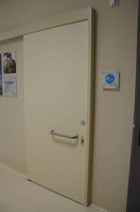 Breite Schiebetür, rechts daneben hängt ein Schild mit dem Logo "Toilette für alle"