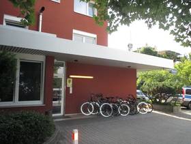 Wohnhaus, im Erdgeschoss Eingang mit einer Stufe davor, der Eingangsbereich ist überdacht und es stehen Fahrräder vor dem Haus