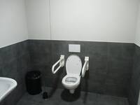 Eine weiße Toilette an einer schwarzen Wand. Auf beiden Seitten sind Haltegriffe