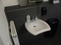 Ein weißes Waschbecken an einer dunklen Wand. Über dem Waschbecken ist ein Spiegel.