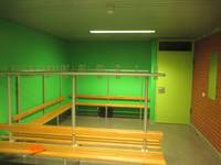 Raum mit mehreren Gaderobenbänken, die linke und die vordere Wand sind grün gestrichen, die Wand rechts ist aus Mauerwerk, in der Wand vorne ist eine helle grüne Tür