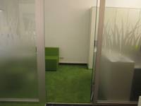 eine offenstehende Tür aus Milchglas, rechts und links ebenfalls Milchglasscheiben, dahinter ein Raum mit einer grünen Bank und grünem Teppichboden