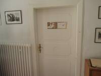 Weiße Holztüre in einer weißen Wand. Links und rechts von der Tür hängen Fotos mit alten Ansichten von Schlierbach.