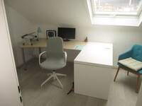 Ein kleiner Raum mit einem Tisch, einem Schreibtischstuhl und einem Sessel mit Holzbeinen