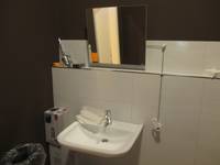 Weißes Waschbecken an einer weiß gekachelter Wand. Über dem Waschbecken ein kippbarer Spiegel.