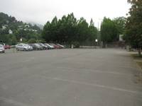 Eine große betonierte Fläche, an der linken Seite ist ein Parkplatz mit parkenden Autos hinter einem Metallzaun der den Festplatz abgrenzt