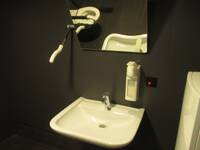 Ein weißes Waschbecken mit einem Seifenspender und einem gekippten Spiegel an einer schwarzen Wand