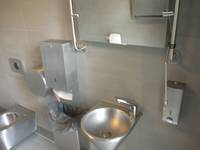 ein Waschbecken das kegelförmig nach unten zuläuft, darüber ein Spiegel, rechts ein Seifenspender, links ein Papiertuchhalter darunter ein Mülleimer, links unten ein Bidet