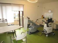 Ein Raum mit einem Tisch, einem Behandlungstuhl und einem Ultraschallgerät auf Rollen