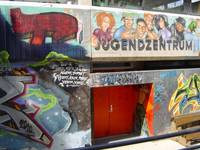 zurückgesetzte roteTür zum Jugendzentrum, an den Wänden rund um den Eingang sind überall Graffitis