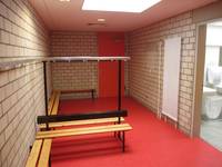Raum mit roten Boden und mehreren Garderobenbänken, rechts Zugang zum Duschbereich 
