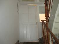 weiße Tür in einer weißen Wand,im rechten Berich Ausschnitt des Treppenhauses mit Holzhandlauf