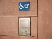 Klingel mit einer Gegensprechanlage. Über der Klingel ist ein blaues Schild mit einem Rollstuhlsymbol und einem Klingelzeichen