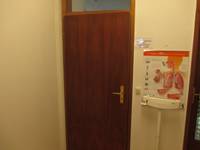 Holztür, rechts davon ist ein Aushang mit einem medizinischen Bild und darunter eine weiße Waage