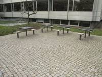 Ein Platz aus Kleinsteinpflaster, in einer der Ecken stehen vier Tische und dabei je zwei montierte Hocker