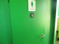 Grüne Tür in einer grünen Wand. Auf de Tür ist ein Schild mit dem SYmbol: Frau und der Aufschrift: Damen.
Darunter ist ein kleiners rundes Schild mit Rollstuhl-Symbol