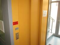 Aufzugstür mit Rahmen, beides orange gestrichen. Taster links am Rahmen