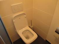 Eine weiße Toilette an einer weiß gekachelten Wand und mit einem dunklen Boden