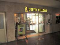 Eine Glasschiebetür mit einem gelbleuchtenden Coffee Fellows Schriftzug über der Tür