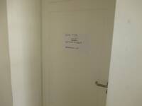 Eine weiße Tür in einer weißen Wand. Auf der Tür ist ein Blatt mit der Aufschrift: "Diese Tür nicht anschließen, Notausgang WC".