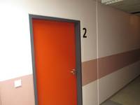 orange Tür in einer hellen Wand mit einem hellrötlichen Streifen, rechtsoben von der Tür die Nummer 2